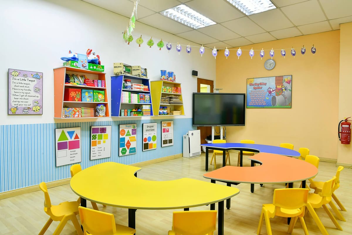 A kindergarten classroom with yellow tables and learning boards